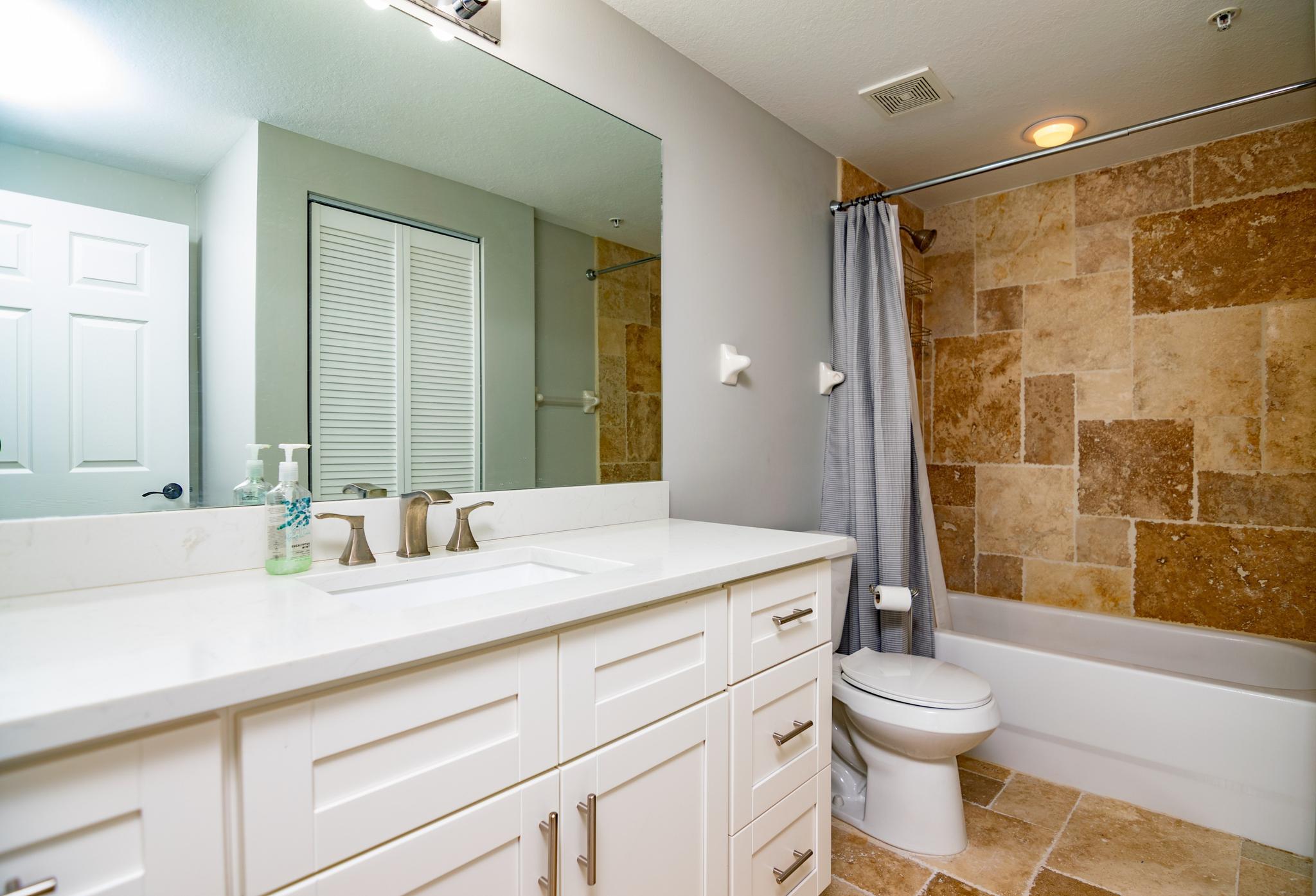 The second full sized bathroom with an updated vanity and travertine tile throughout